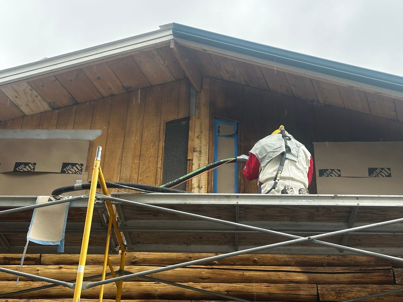 Crew member on scaffolding sandblasting the board siding on a log home gable, Idaho