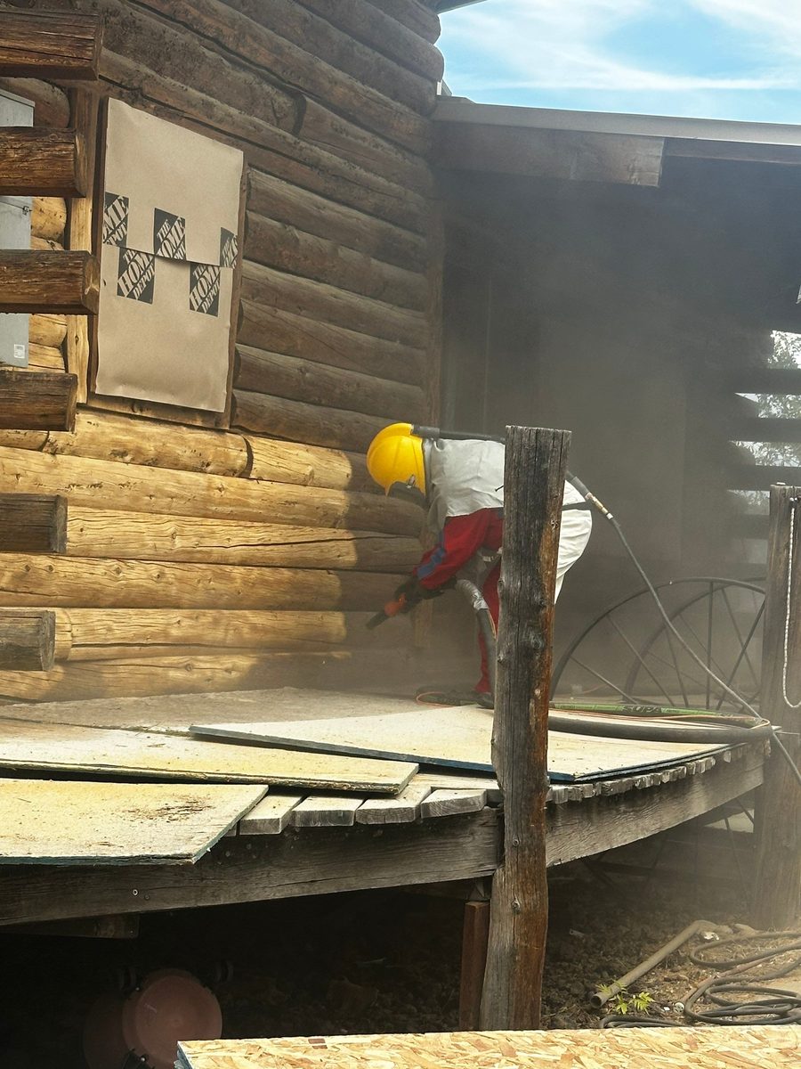 Chase Construction crew member in a supplied-air hood media blasting a log wall in Idaho