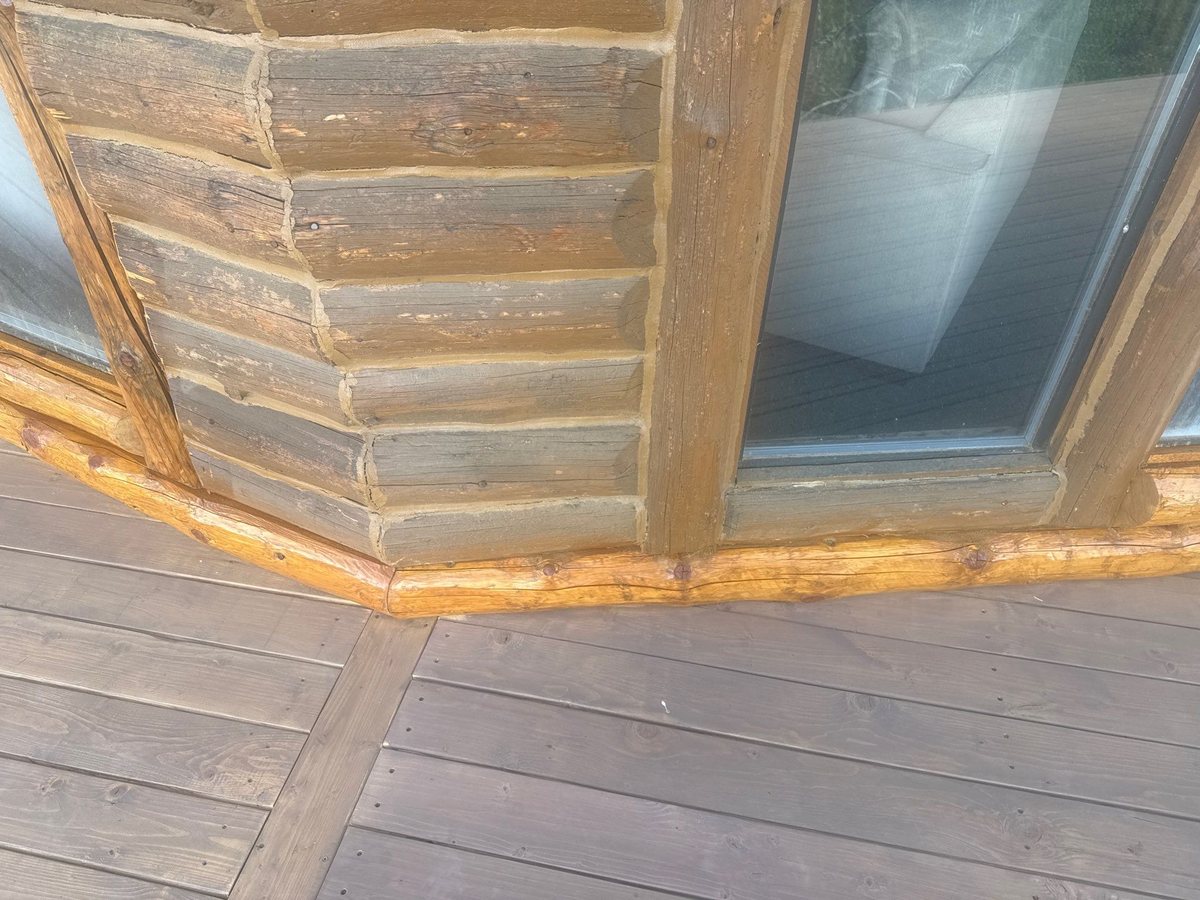 A new, freshly stained bottom log running along the deck line beneath older weathered logs on an Idaho log home