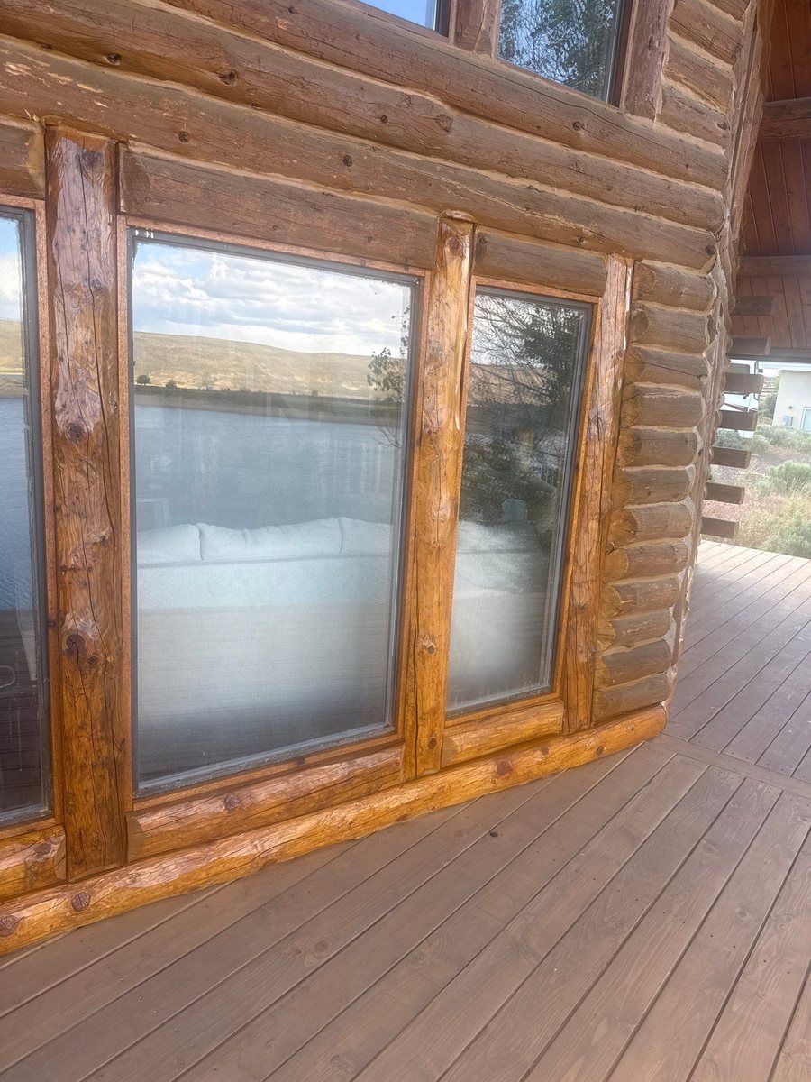 A log wall with tall windows above a deck, with new lower logs and fresh stain along the sill line