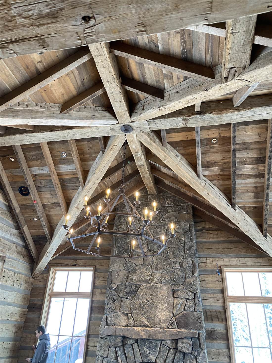 Hand-hewn timber trusses over a great room with an iron chandelier and stone fireplace